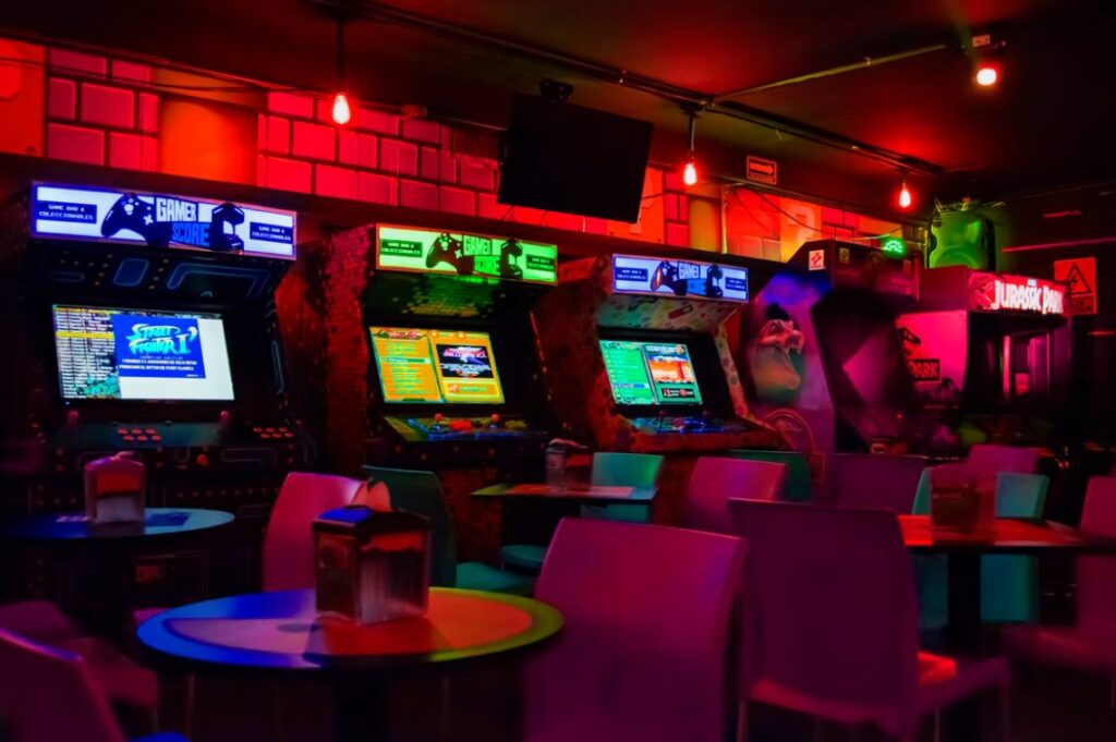 arcade machines near tables and chairs in dim lit